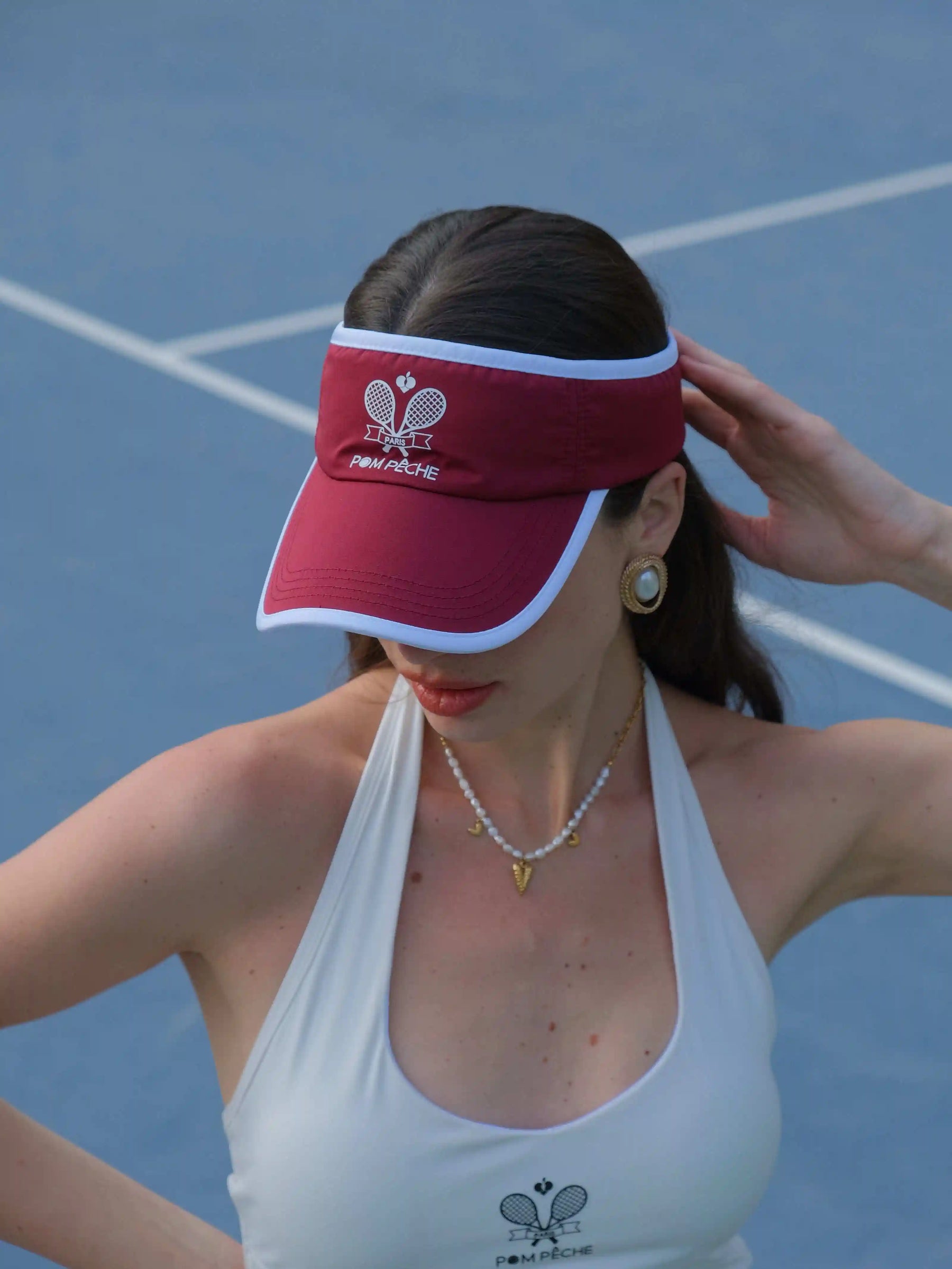 Woman wearing a red visor and white tennis outfit on a tennis court
