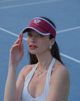 Woman wearing a red visor and white tank top on a tennis court
