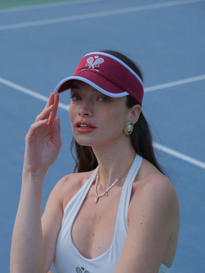 Red tennis visor with embroidered Pom Pêche logo, white trim, worn on the court.