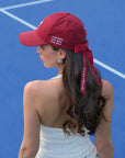 Deep red tennis baseball cap with embroidered Pom Pêche logo and detachable ribbon.