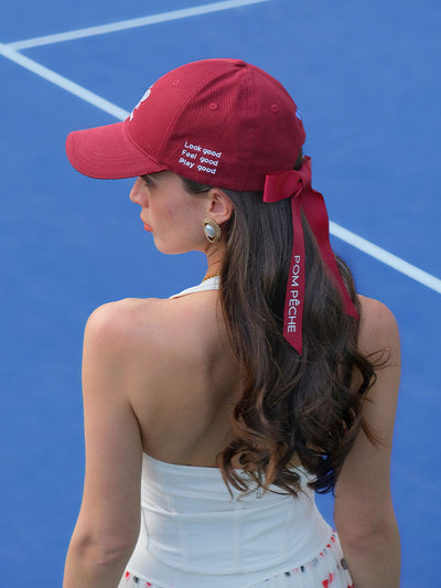Deep red tennis baseball cap with embroidered Pom Pêche logo and detachable ribbon.