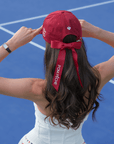 Deep red tennis baseball cap with embroidered Pom Pêche logo and detachable ribbon.
