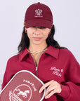 Wine red tennis cap with embroidered logo and adjustable ribbon on the back strap.