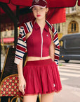Woman in a red outfit with a striped jacket standing under a red umbrella in an urban setting.