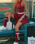 Person in a red tennis outfit sitting on a bench with a racket, wearing white shoes and red socks.
