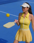 Woman in yellow dress and visor playing pickleball on a blue court
