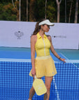 Woman in a yellow tennis outfit standing on a tennis court with a racket and visor.
