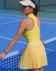 Woman in a yellow dress and white visor standing on a blue tennis court.