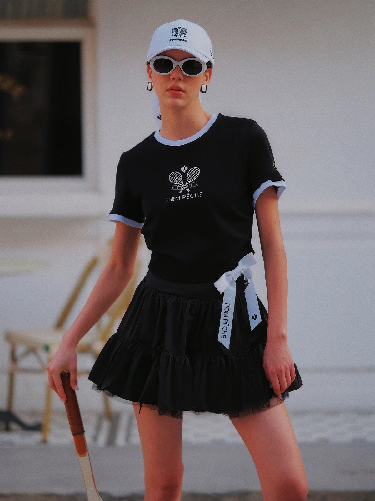 Contrast Trim Tennis Tee black, full outfit with black ruffle tennis skirt, white Pom Pêche bow, Pom Pêche cap and sunglasses, Paris editorial