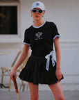 Contrast Trim Tennis Tee black, full outfit with black ruffle tennis skirt, white Pom Pêche bow, Pom Pêche cap and sunglasses, Paris editorial