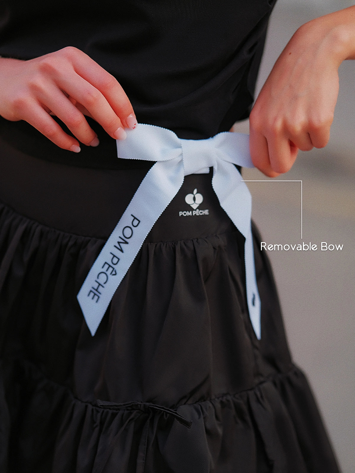 Contrast Trim Tennis Tee black – removable Pom Pêche white ribbon bow detail at waist, feminine sporty accent