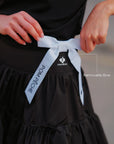 Contrast Trim Tennis Tee black – removable Pom Pêche white ribbon bow detail at waist, feminine sporty accent