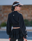 Cropped UV tennis jacket back view in black, fitted waist cinch design with lightweight sporty silhouette