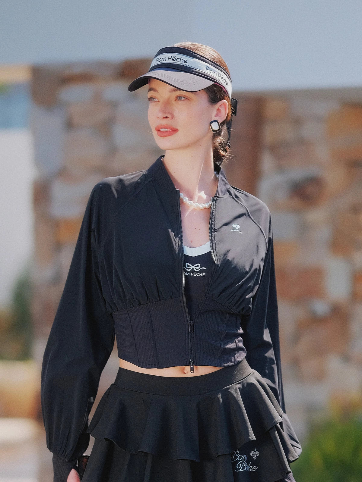 Black cropped UV tennis jacket styled front view, dual zipper waist cinch design for sculpted sporty silhouette
