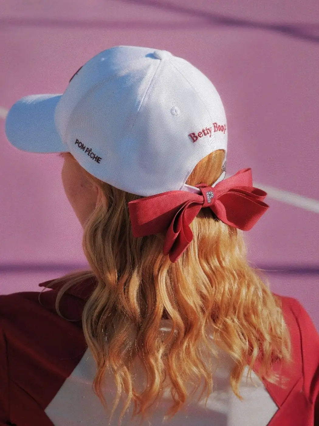 Person wearing a white cap with a red bow on a pink background