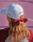 Person wearing a white cap with a red bow on a pink background