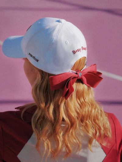 Person wearing a white cap with a red bow on a pink background