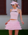 Pink Bow Halter Tennis Top worn with pink ruffle tennis skirt and Pom Pêche visor, full court-ready outfit on grass court
