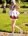 Pom Pêche 750ml Insulated Tumbler in black and white harlequin – model walking in Paris garden holding tumbler and Pom Pêche Racquet Club canvas tote bag with tennis racket, styled with white Poise polo halter top, Pom Pêche La Rose mirror visor, white tennis sneakers and Pom Pêche rose embroidered socks