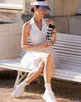 Pom Pêche 750ml Insulated Tumbler with Straw Lid in black and white harlequin – model holding tumbler with both hands on Paris garden white bench, black straw lid and braided carry strap detail, styled with white Poise polo halter top, Pom Pêche La Rose mirror visor and white tennis sneakers