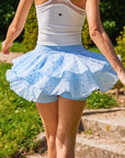 Pom Pêche x Betty Boop Cake Skirt in Paris blue – back view showing double-layer polka dot mesh ruffle tiers with built-in blue shorts visible, wide sky blue high waistband with Pom Pêche heart logo, styled with white ribbed tank in garden