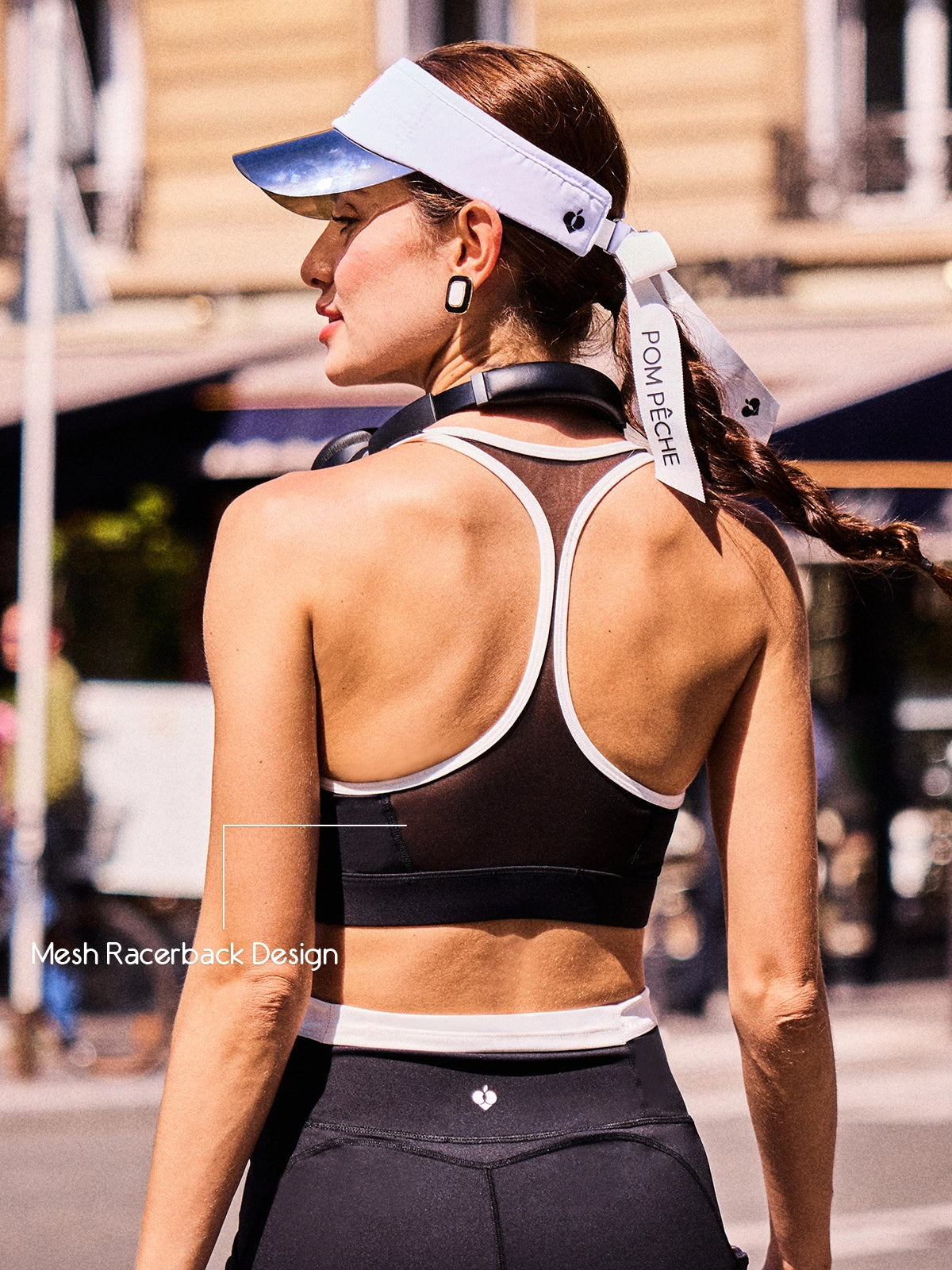 Back view of Pom Pêche x Betty Boop black tank top highlighting breathable mesh racerback design and white contrast trim, worn with Pom Pêche visor on Paris street