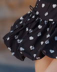Macro detail of Pom Pêche black Bubble A-Line Skirt showing voluminous bubble hem structure with white heart and Pom Pêche logo allover print – structured polyester-spandex fabric