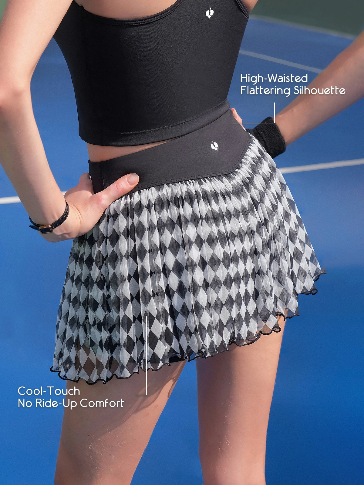 Pom Pêche black Diamond Mesh Skirt feature callout – High-Waisted Flattering Silhouette and Cool-Touch No Ride-Up Comfort annotated, showing wide black waistband with Pom Pêche crown logo and harlequin mesh skirt on blue court