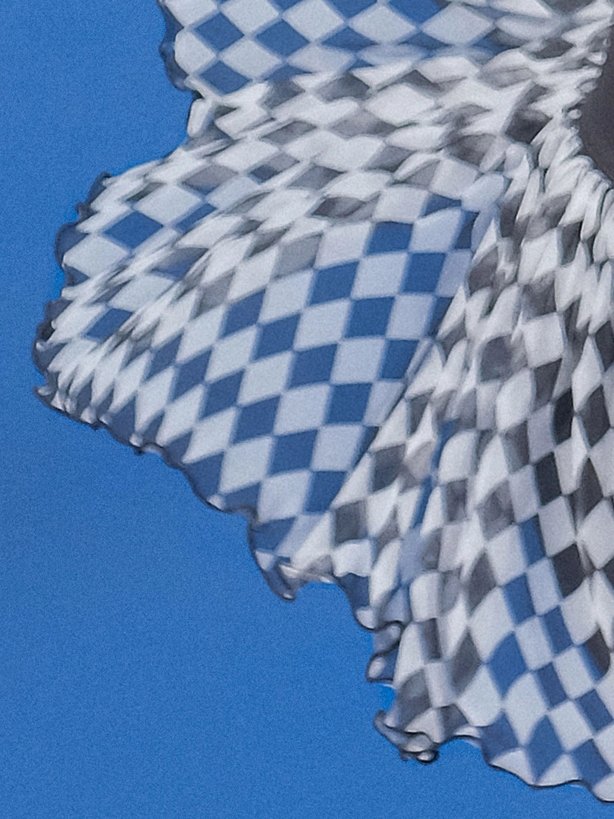 Macro aerial detail of Pom Pêche black Diamond Mesh Skirt showing black and white harlequin diamond print high-density mesh tulle flying against blue sky – ultra-lightweight 0.3g UPF 50+ LYCRA® cool-touch fabric