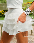 Close-up of Pom Pêche white Mille Tiered Skirt showing 4 hidden pockets in built-in shorts, model pulling skirt layer to reveal pocket – styled with Pom Pêche striped wristband