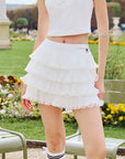 Pom Pêche white Mille Tiered Skirt feature callout – high waist A-line silhouette with Pom Pêche logo and 4-layer light fine tulle pleats annotated, Paris garden background