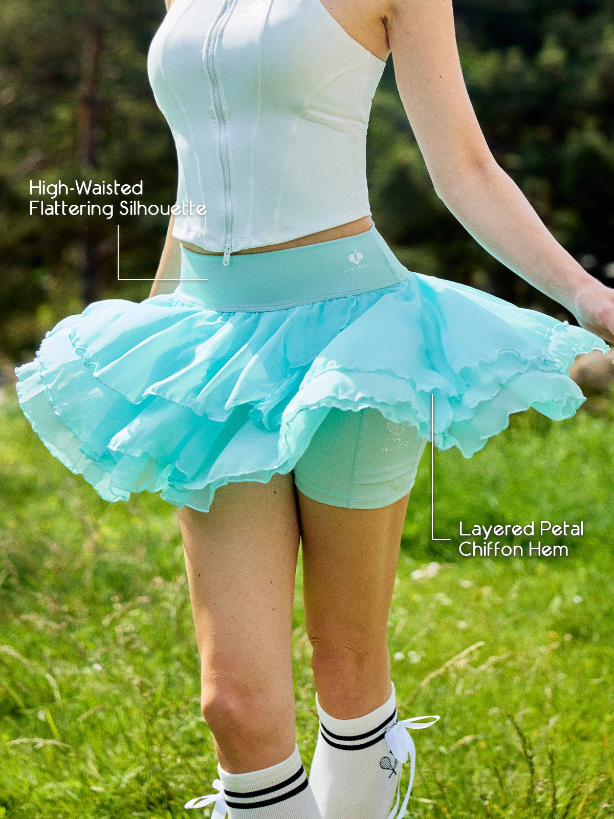 Pom Pêche mint green Petal Tiered Skirt feature callout – High-Waisted Flattering Silhouette and Layered Petal Chiffon Hem annotated, showing voluminous three-tier chiffon skirt with built-in shorts on outdoor grass