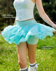 Pom Pêche mint green Petal Tiered Skirt feature callout – High-Waisted Flattering Silhouette and Layered Petal Chiffon Hem annotated, showing voluminous three-tier chiffon skirt with built-in shorts on outdoor grass