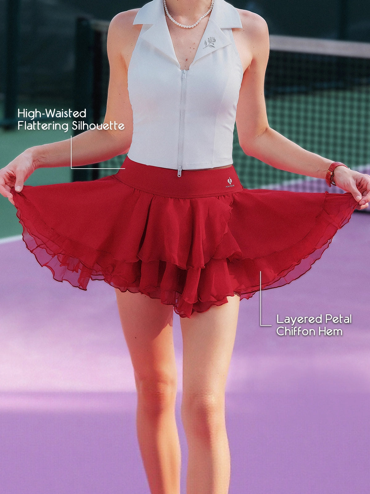 Pom Pêche wine red Petal Tiered Skirt feature callout – High-Waisted Flattering Silhouette and Layered Petal Chiffon Hem annotated, model holding out three-tier chiffon skirt showing full A-line silhouette on purple clay court