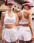 Pom Pêche Poise™ Mesh Back Tank Top in white – front and back view showing Deep U neckline with Pom Pêche Sports Club Paris burgundy script print and sheer mesh racerback design, styled with white Sports Club shorts, pink Pom Pêche visor and pearl necklace on Paris street