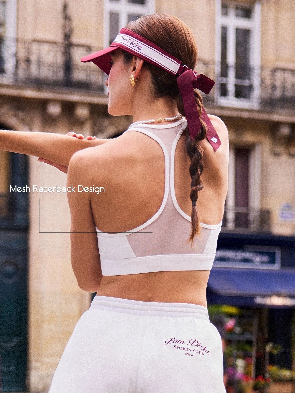 Back view of Pom Pêche white Poise™ Mesh Back Tank with Mesh Racerback Design callout – sheer mesh panel with Y-shaped racerback straps for breathability and unrestricted movement, styled with burgundy bow hair ribbon and pearl necklace on Paris street