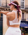 Back view of Pom Pêche white Poise™ Mesh Back Tank with Mesh Racerback Design callout – sheer mesh panel with Y-shaped racerback straps for breathability and unrestricted movement, styled with burgundy bow hair ribbon and pearl necklace on Paris street