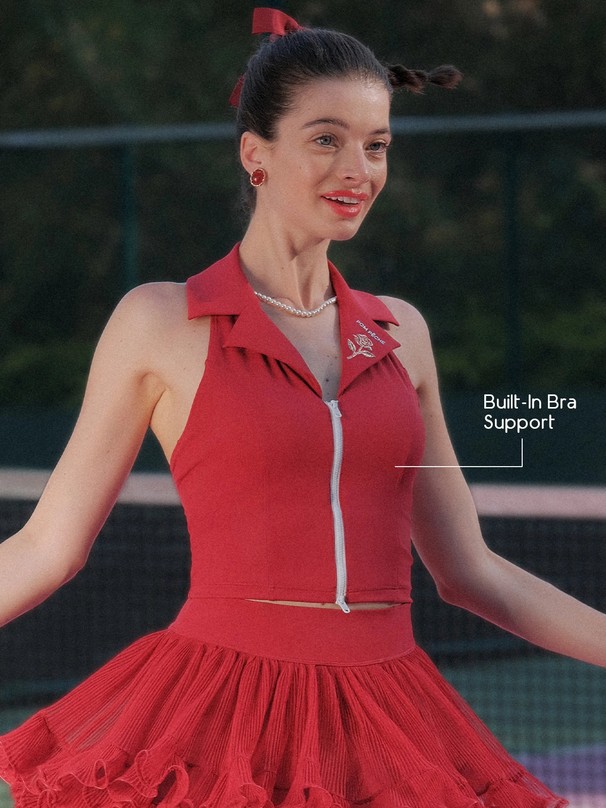 Pom Pêche Paris red Poise™ Rose Halter Polo Tank with Built-In Bra Support callout – model spinning showing polo collar, Pom Pêche rose embroidery and dual-zipper front, styled with wine red ruffle skirt on outdoor court