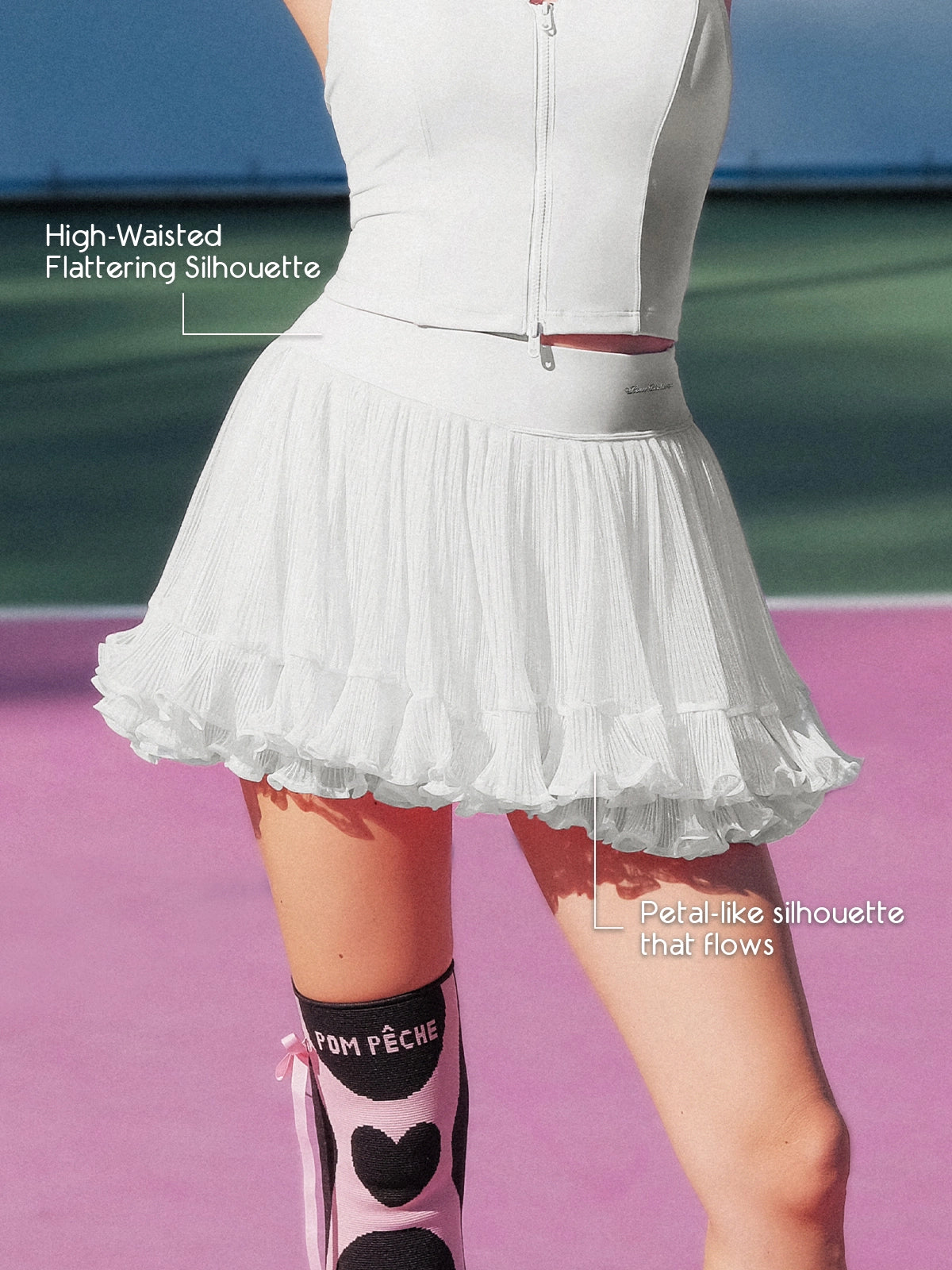 Pom Pêche white Rose Ruffle Skirt feature callout – High-Waisted Flattering Silhouette and Petal-like silhouette that flows annotated, showing airy pleated mesh hem and Pom Pêche logo waistband on pink court