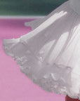 Macro detail of Pom Pêche white Rose Ruffle Skirt showing fine pleated airy mesh outer layer with double-tier petal-like scalloped ruffle hem flaring in motion – lightweight cool-touch UPF 50+ fabric