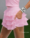 Close-up of Pom Pêche pink Ruffle Cake Skirt showing 4 hidden pockets in built-in shorts, model pulling tulle layer to reveal pocket access – styled with Pom Pêche striped wristband