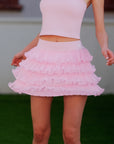 Pom Pêche Ruffle Cake Skirt in blush pink – 5-layer light fine tulle ruffle tiers creating voluminous A-line silhouette, high-waist band, styled with matching pink crop tank on grass court