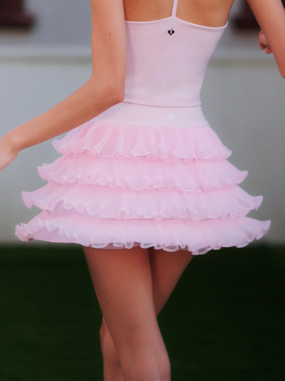 Back view of Pom Pêche pink Ruffle Cake Skirt – 5-layer tulle ruffle tiers flaring with movement, styled with Pom Pêche crown logo pink crop tank on outdoor grass court