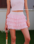 Pom Pêche pink Ruffle Cake Skirt feature callout – high waist A-line silhouette and 4-layer light fine tulle pleats annotated, model holding tennis racket on grass court