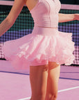Pom Pêche Spin™ Petal Tiered Tennis Skirt in light pink – three-layer petal chiffon hem with built-in shorts visible, high-waisted band, styled with matching zip halter top on pink court