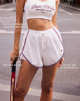 Pom Pêche white women's tennis shorts with elastic adjustable drawstring waistband, high side-slit hem and contrast tricolor stripe – key features annotated