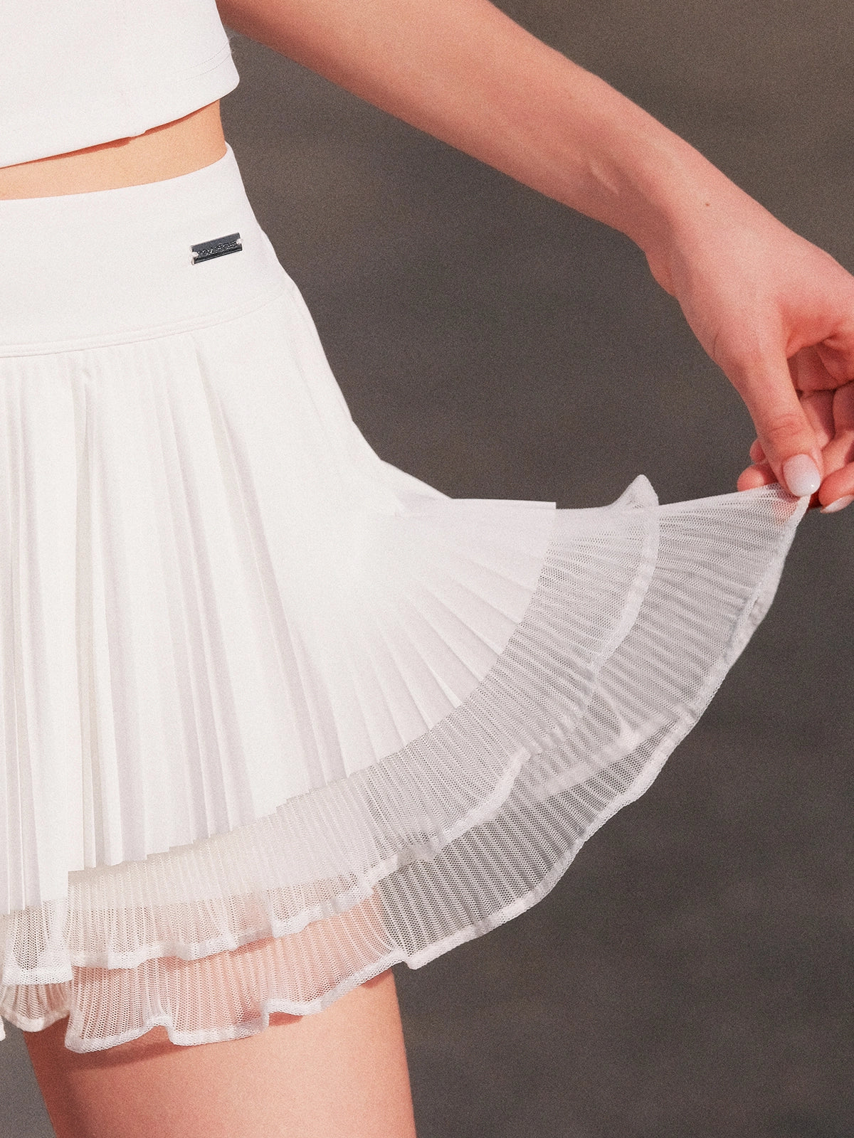 Macro detail of Pom Pêche white Waltz Layered Tennis Skirt showing double-layer construction – outer fine pleated LYCRA® layer over inner semi-sheer mesh ruffle scalloped hem, smooth anti-static 4-way stretch fabric