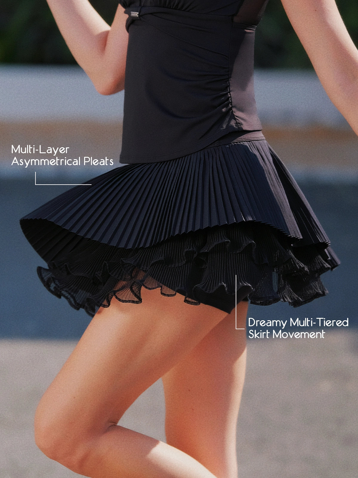 Pom Pêche black Waltz Skirt feature callout – multi-layer asymmetrical pleats and dreamy multi-tiered skirt movement annotated, showing fluid dynamic silhouette during motion