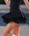 Pom Pêche black Waltz Skirt feature callout – multi-layer asymmetrical pleats and dreamy multi-tiered skirt movement annotated, showing fluid dynamic silhouette during motion