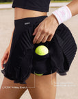 Close-up of Pom Pêche black Waltz tennis skirt showing LYCRA® 4-way stretch built-in shorts with four side pockets holding 8 tennis balls – Pom Pêche metallic logo waistband detail